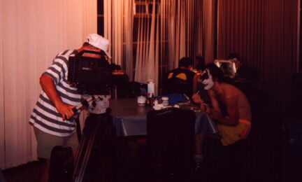 A camera operator films a band member at a table.
