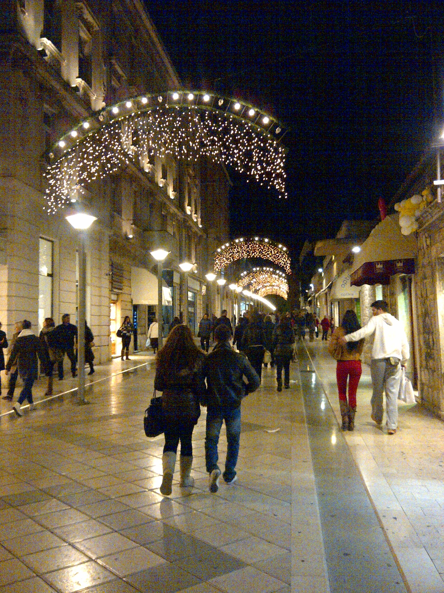 Holiday light arches over a busy pedestrian street at night