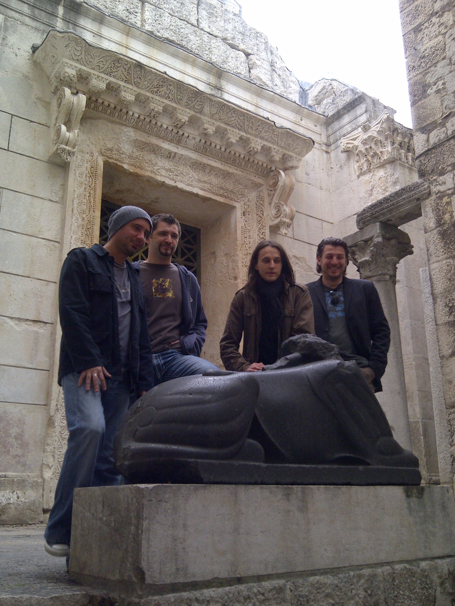 Four friends posing around a sculpture in a historic stone courtyard
