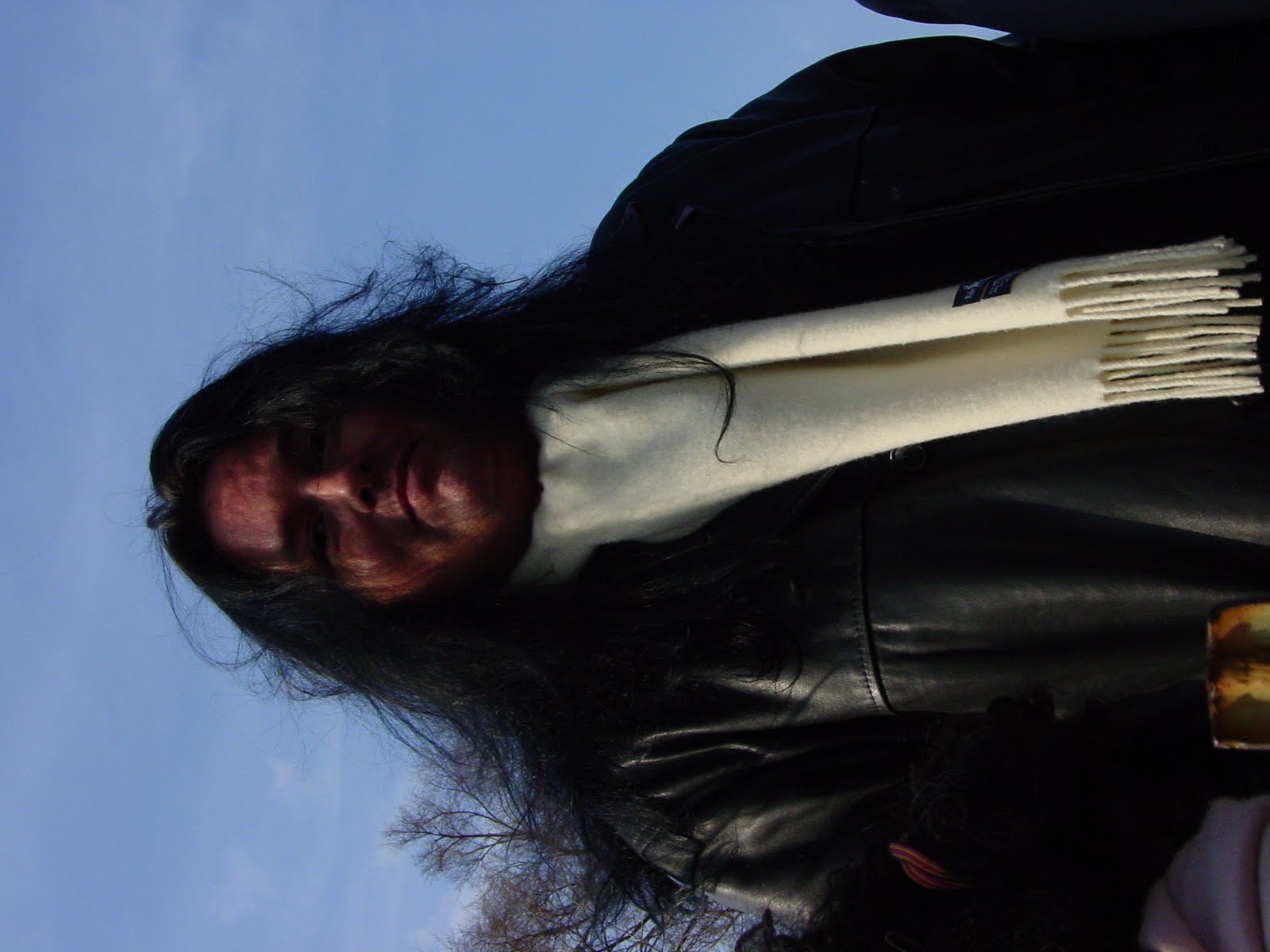 Benny upright in a black winter coat and white scarf beneath bare trees