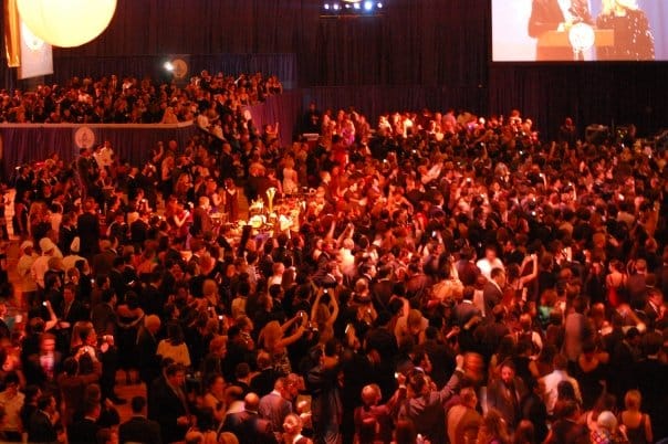 A large indoor crowd at the Youth Ball under warm red stage lighting