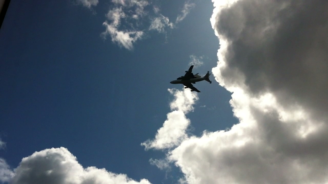 Space Shuttle Enterprise mounted on a NASA 747 passes through the clouds above Benny Doro's apartment.