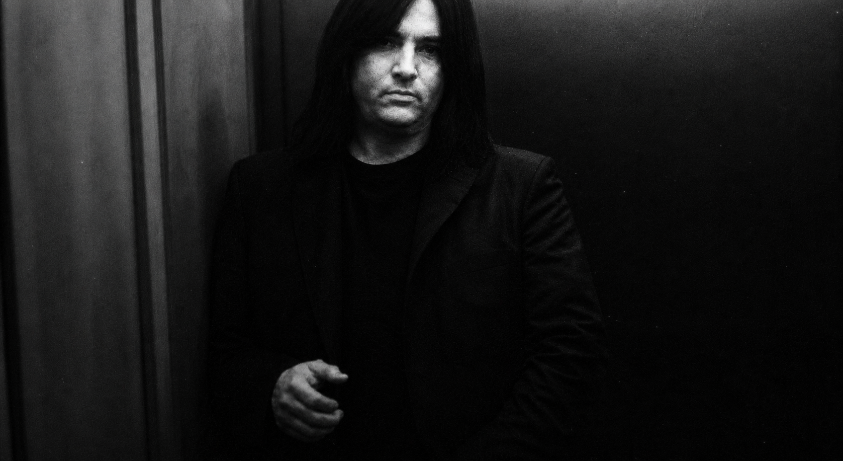 A black-and-white portrait of Benny Doro standing thoughtfully in a dark interior