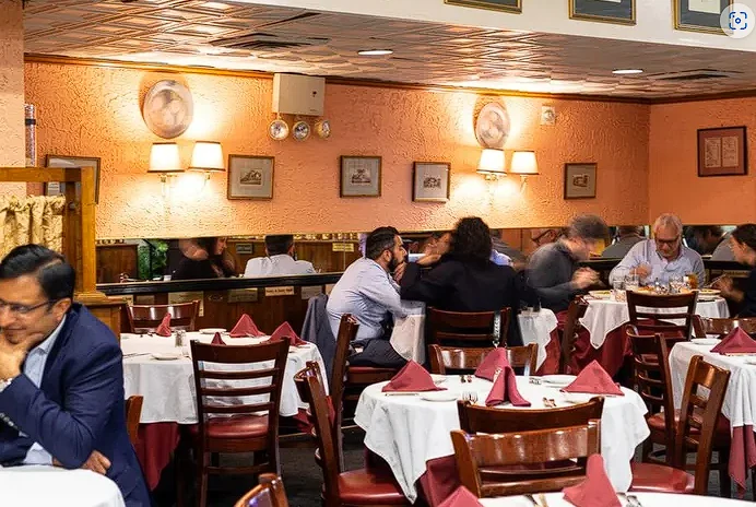 The warmly lit dining room at Pietro’s with white tablecloths and red napkins
