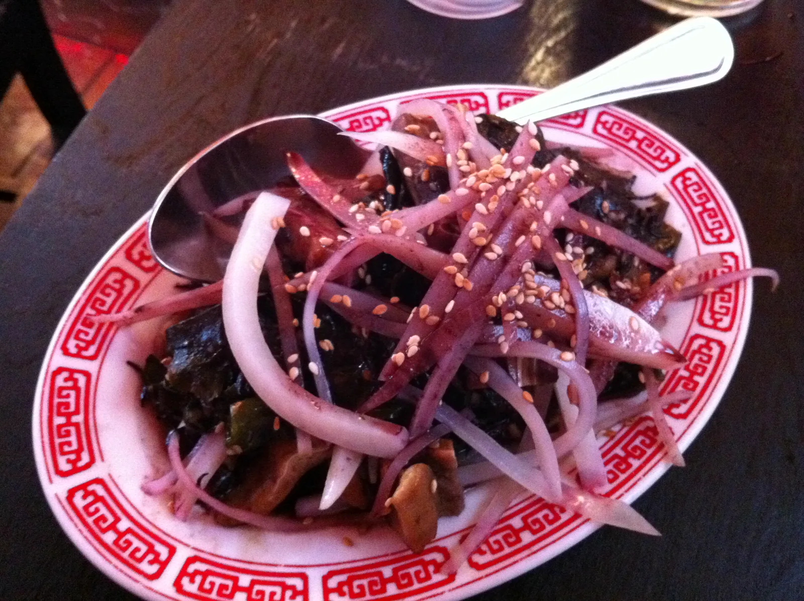 A dark vegetable dish topped with red onion and sesame