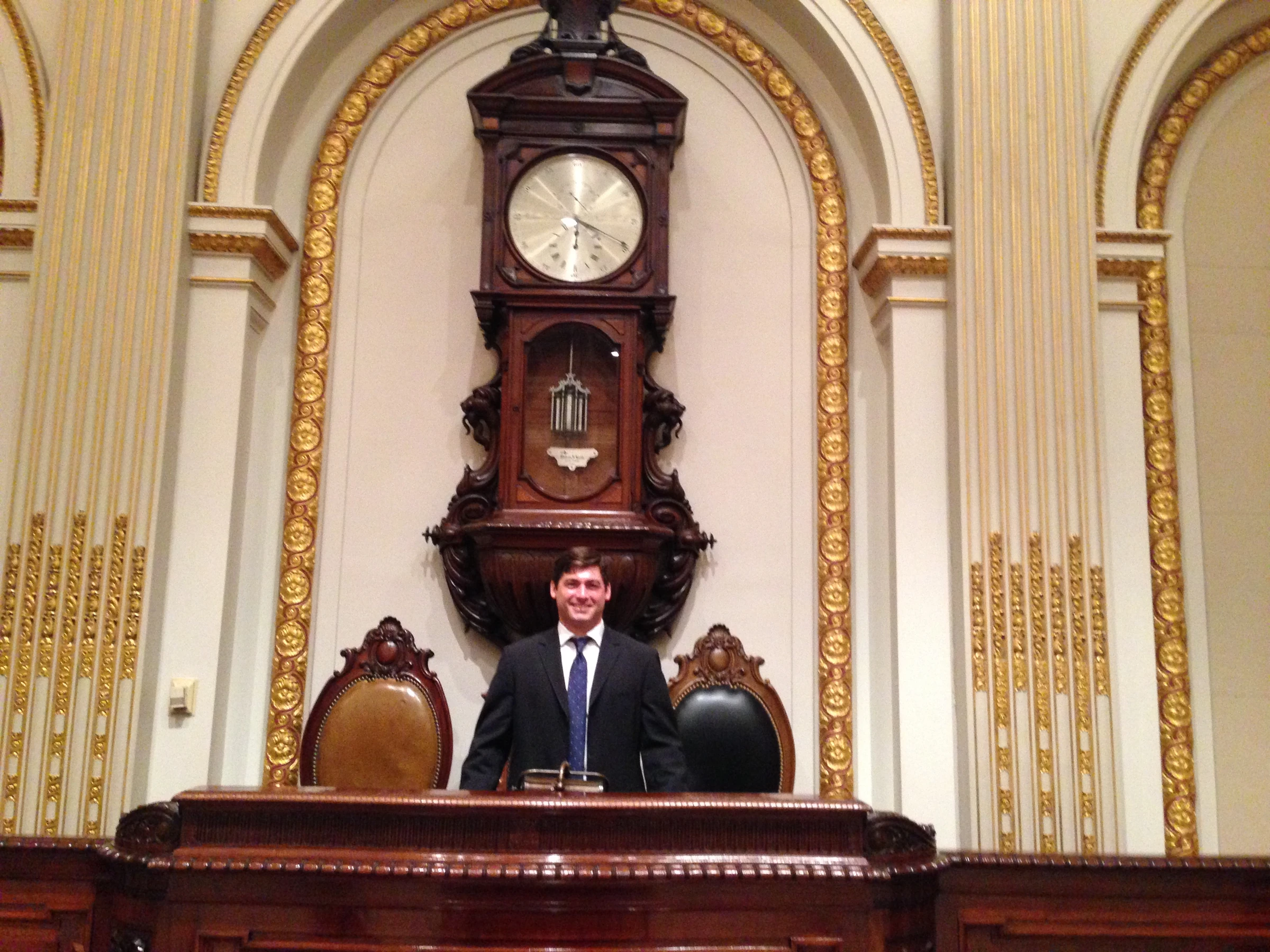Adam Pasquale standing behind the historic NYSE rostrum beneath the antique clock