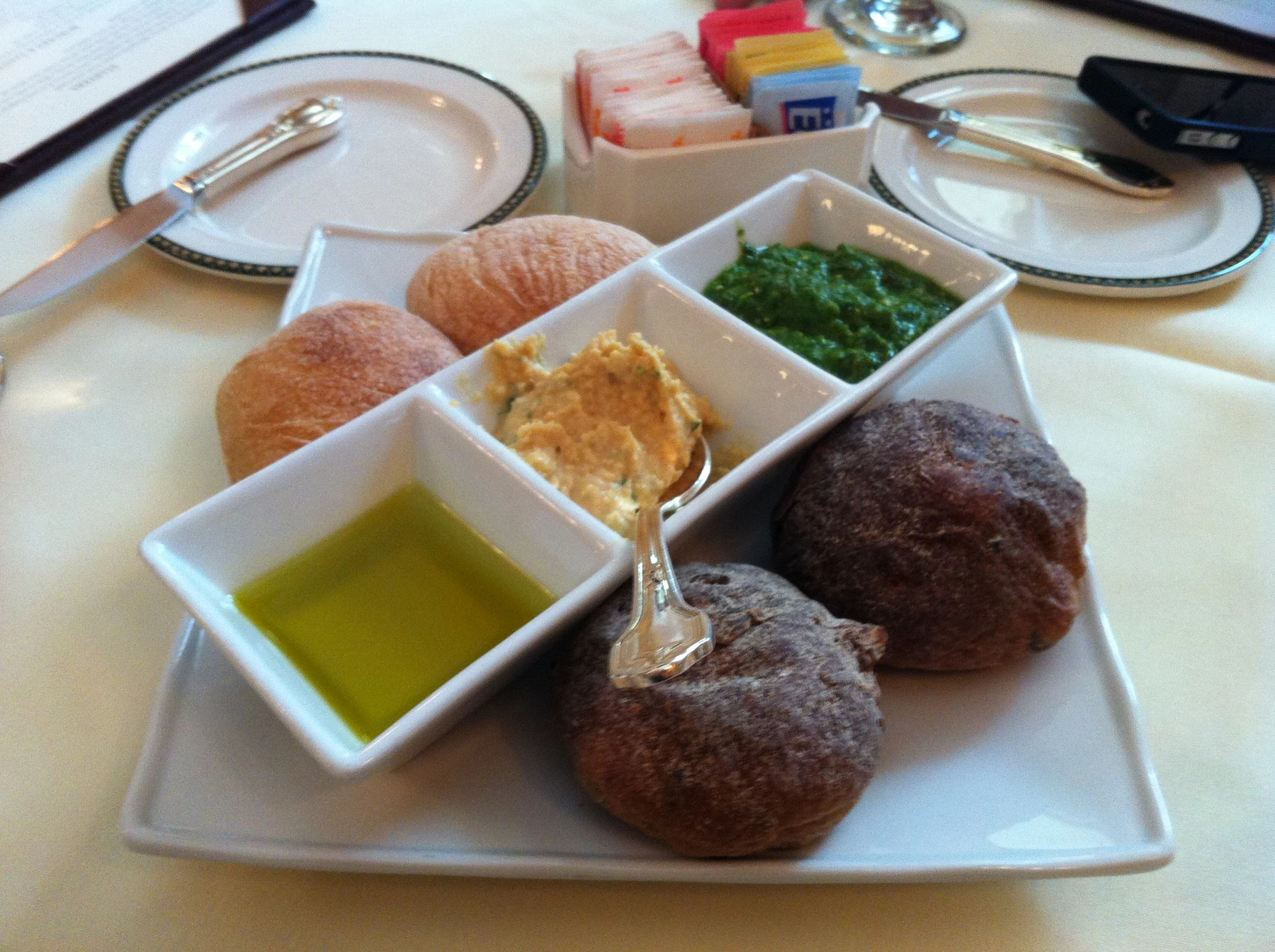 Textured dark rolls beside olive oil, hummus and pesto