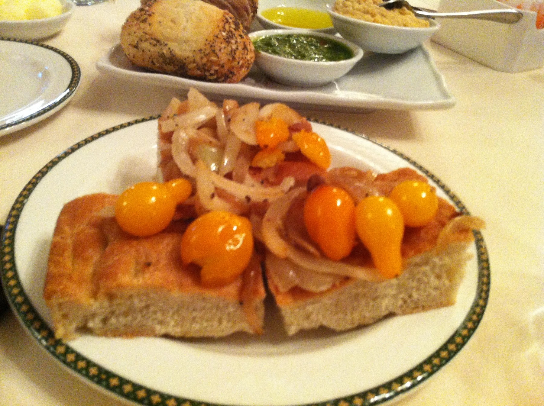 Focaccia topped with onions and small golden tomatoes on a plate at 1792