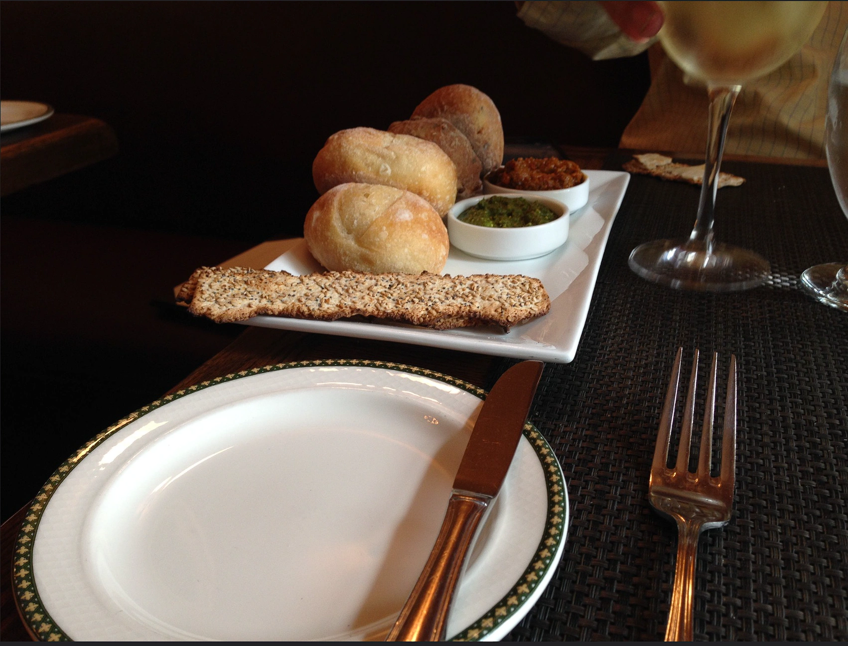 An empty dinner plate with bread service, dips and glassware beyond it at 1792