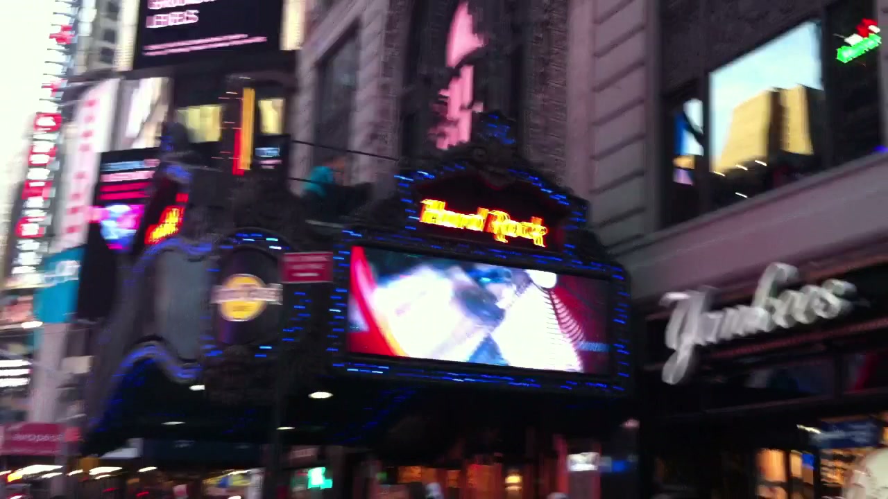 Times Square screens and storefronts seen from the sidewalk.